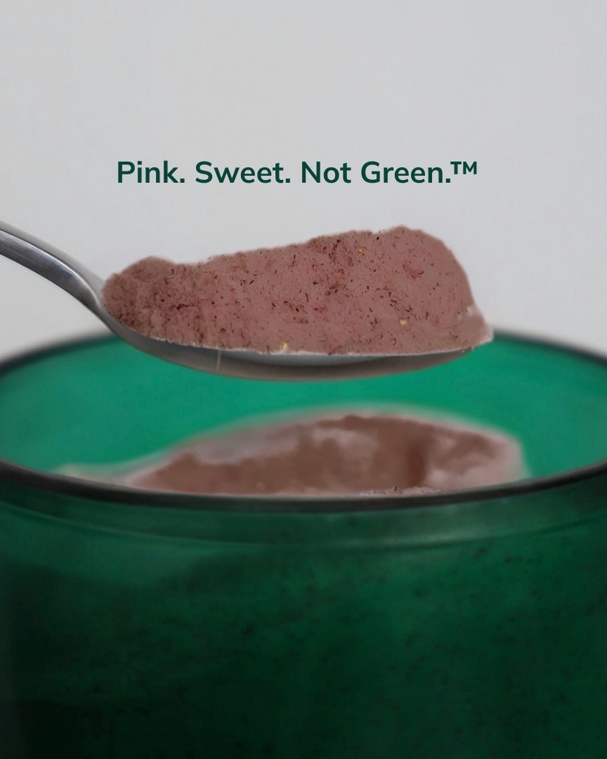 Spoonful of Gut Ritual+ powder, a pinky-brown colour, above the green glass vessel