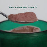 Spoonful of Gut Ritual+ powder, a pinky-brown colour, above the green glass vessel